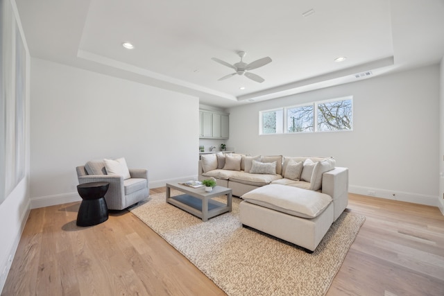 living room with light wood finished floors, visible vents, baseboards, and a raised ceiling