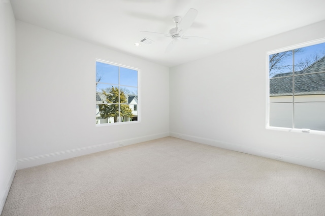 empty room featuring light carpet, visible vents, a ceiling fan, and baseboards