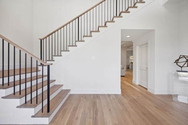 stairway featuring a high ceiling, recessed lighting, wood finished floors, and baseboards