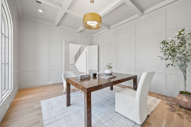 dining space featuring light wood finished floors, coffered ceiling, stairway, beamed ceiling, and a decorative wall