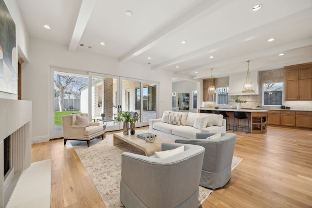 living room with beamed ceiling, a fireplace, light wood-style flooring, and a healthy amount of sunlight