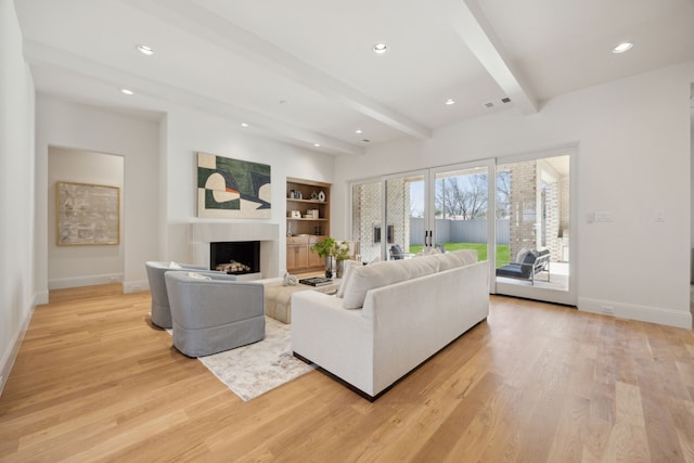 living area with visible vents, baseboards, light wood-style flooring, and beam ceiling