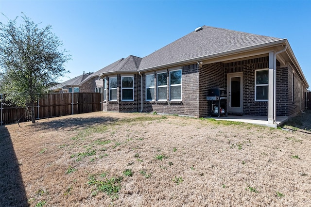 rear view of property with a patio area, a shingled roof, fence, and brick siding