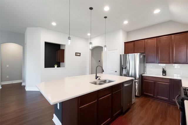 kitchen featuring arched walkways, a center island with sink, light countertops, appliances with stainless steel finishes, and a sink