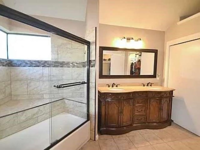 bathroom with bath / shower combo with glass door, double vanity, a sink, and tile patterned floors