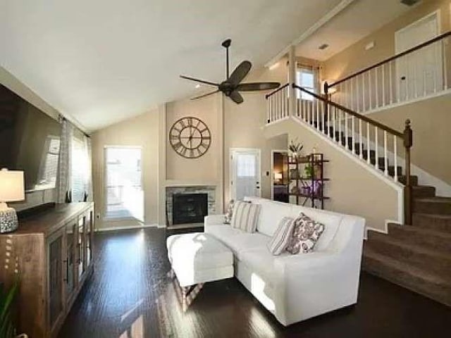 living room featuring ceiling fan, stairway, dark wood-style flooring, a fireplace, and high vaulted ceiling