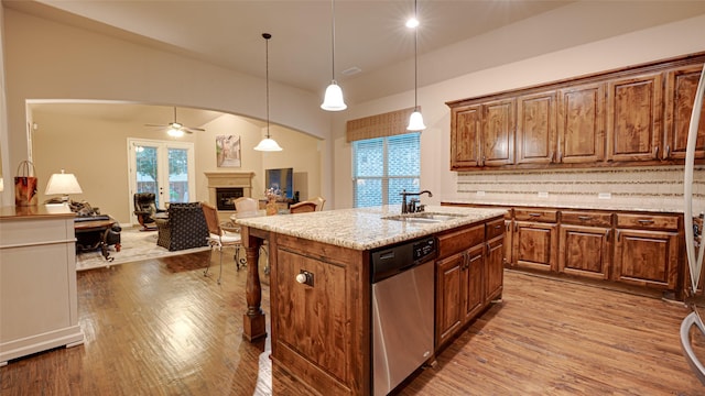 kitchen with arched walkways, a center island with sink, a fireplace, a sink, and dishwasher