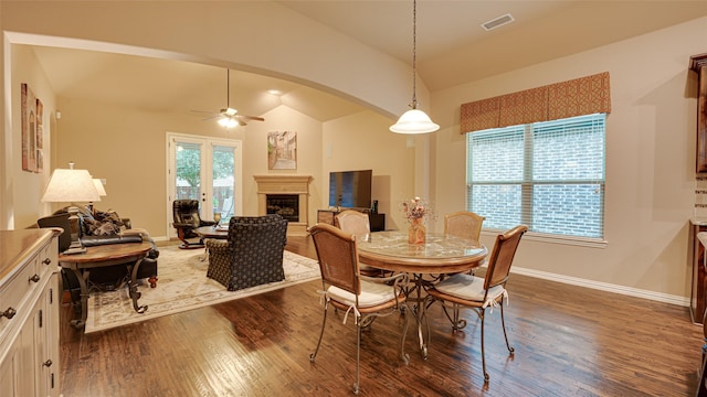 dining space with a fireplace with raised hearth, arched walkways, dark wood-style flooring, visible vents, and vaulted ceiling