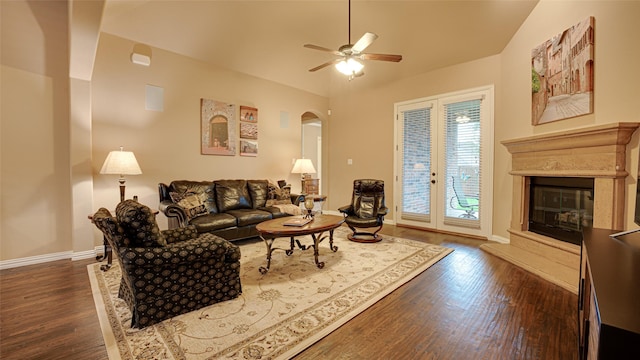 living room with dark wood-style floors, arched walkways, a ceiling fan, a glass covered fireplace, and baseboards