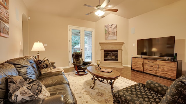 living area featuring baseboards, a glass covered fireplace, lofted ceiling, ceiling fan, and wood finished floors