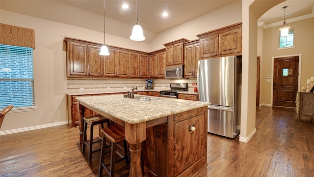 kitchen featuring a kitchen island with sink, stainless steel appliances, a sink, decorative backsplash, and dark wood finished floors