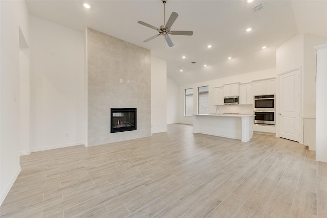 unfurnished living room featuring ceiling fan, recessed lighting, a tiled fireplace, and light wood-style floors