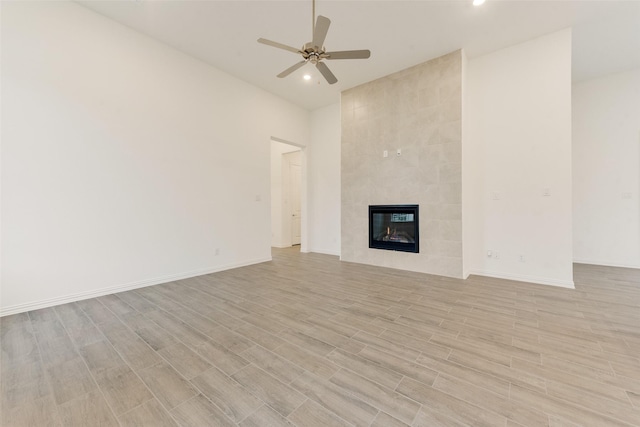 unfurnished living room featuring a ceiling fan, baseboards, a fireplace, and light wood finished floors