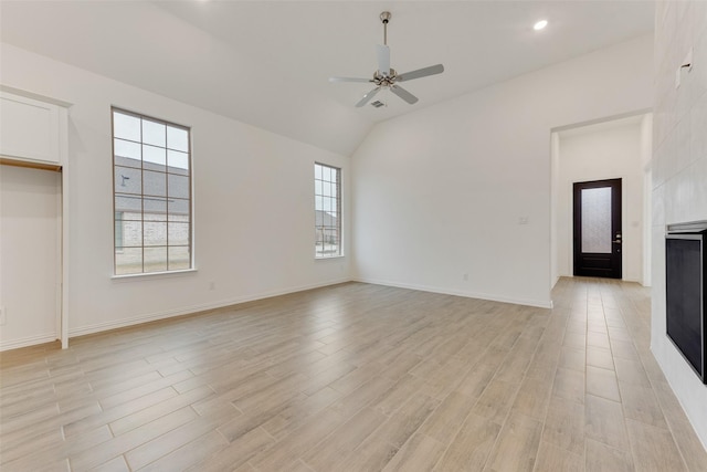 unfurnished room featuring a large fireplace, baseboards, ceiling fan, vaulted ceiling, and light wood-type flooring