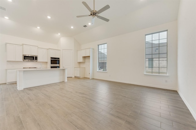 kitchen with tasteful backsplash, white cabinets, light wood-style flooring, appliances with stainless steel finishes, and open floor plan