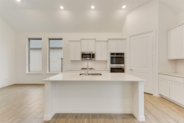 kitchen featuring lofted ceiling, appliances with stainless steel finishes, light countertops, light wood-type flooring, and a sink