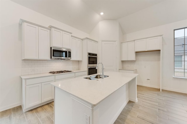 kitchen with lofted ceiling, appliances with stainless steel finishes, backsplash, a kitchen island with sink, and a sink