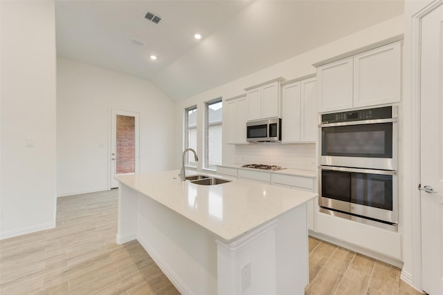 kitchen with lofted ceiling, a sink, visible vents, appliances with stainless steel finishes, and an island with sink