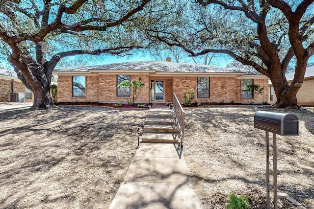 single story home with central AC, brick siding, and roof with shingles