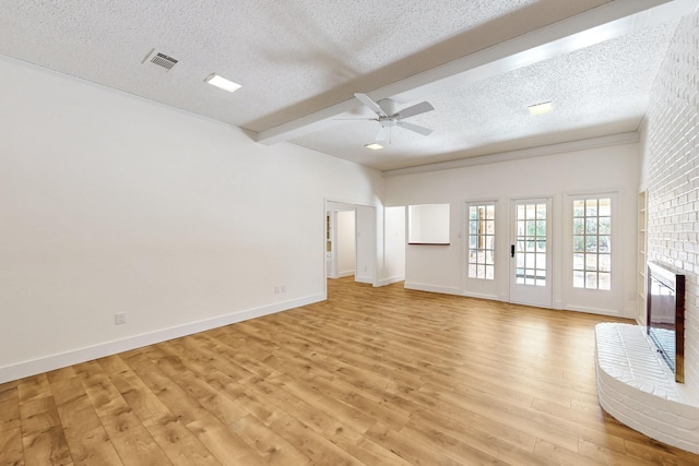 unfurnished living room featuring beam ceiling, light wood-style floors, a brick fireplace, a textured ceiling, and baseboards