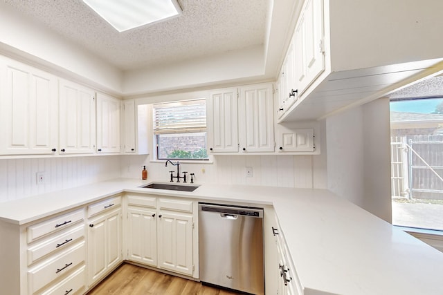 kitchen with stainless steel dishwasher, light wood-type flooring, light countertops, a textured ceiling, and a sink