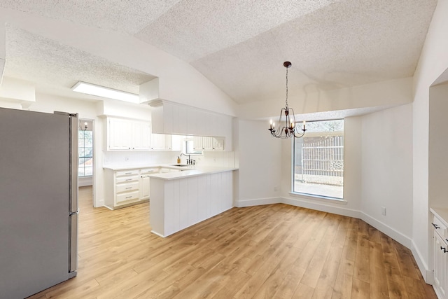 kitchen with a peninsula, a sink, light countertops, freestanding refrigerator, and light wood finished floors