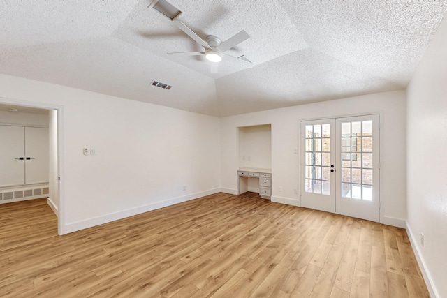 spare room featuring light wood finished floors, visible vents, vaulted ceiling, a textured ceiling, and french doors