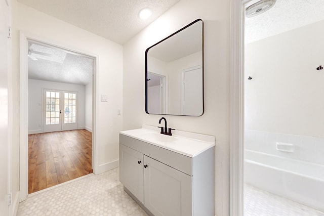 full bathroom featuring vanity, a bathing tub, a textured ceiling, french doors, and baseboards