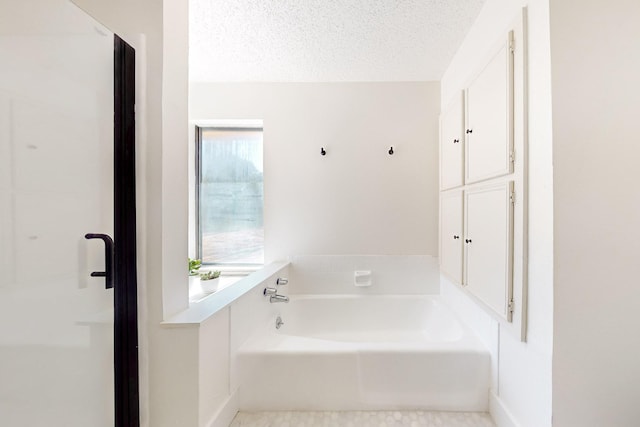bathroom featuring a textured ceiling, baseboards, and a bath