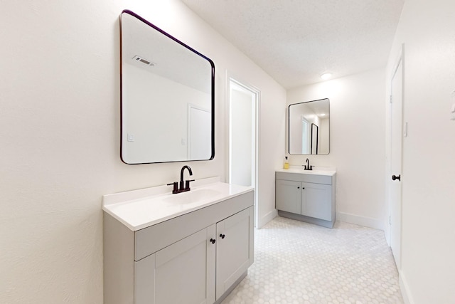 bathroom with two vanities, a sink, a textured ceiling, and baseboards