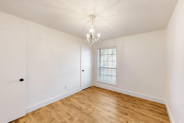 empty room with light wood finished floors, baseboards, a textured ceiling, and an inviting chandelier