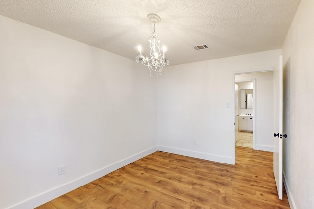 empty room with a textured ceiling, a chandelier, visible vents, baseboards, and light wood-type flooring