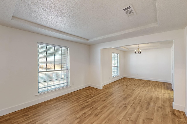 unfurnished room featuring light wood-type flooring, visible vents, and a tray ceiling