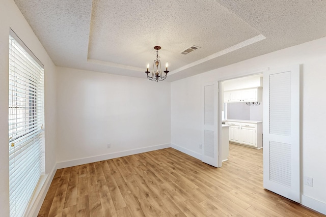 empty room featuring light wood-style floors, visible vents, a raised ceiling, and a textured ceiling