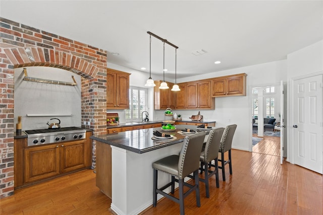 kitchen featuring stainless steel gas cooktop, a kitchen island, a sink, light wood-style floors, and brown cabinets