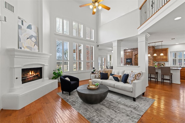 living area featuring a ceiling fan, a lit fireplace, decorative columns, and light wood-style flooring