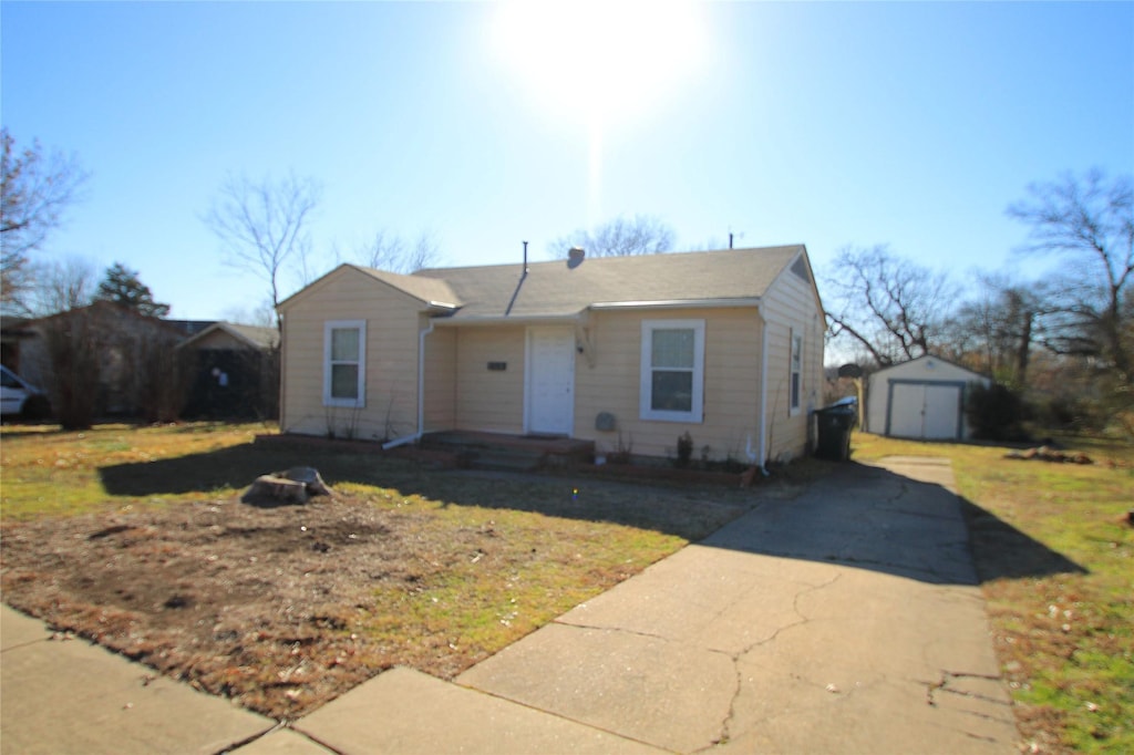 bungalow-style home with a garage, a front lawn, concrete driveway, and an outbuilding