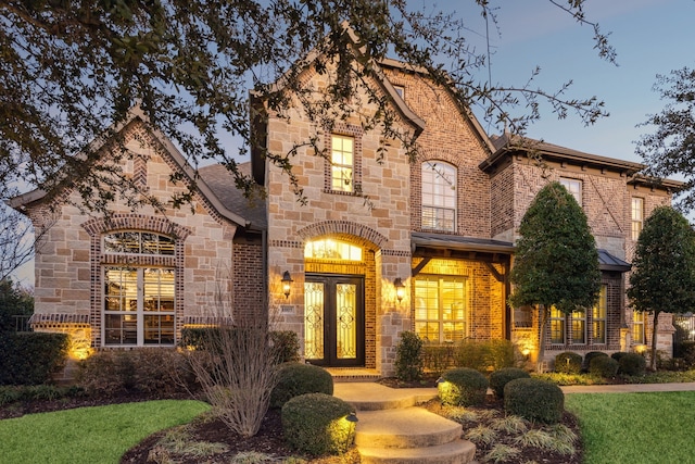 french country style house with stone siding, french doors, brick siding, and roof with shingles