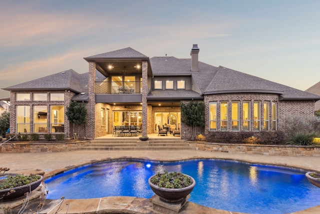 pool at dusk with an outdoor pool and a patio