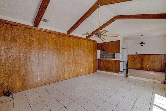 unfurnished living room with wooden walls, visible vents, ceiling fan, vaulted ceiling with beams, and a sink