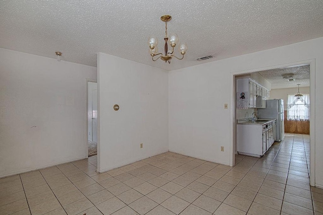 unfurnished dining area with light tile patterned floors, visible vents, an inviting chandelier, a textured ceiling, and a sink