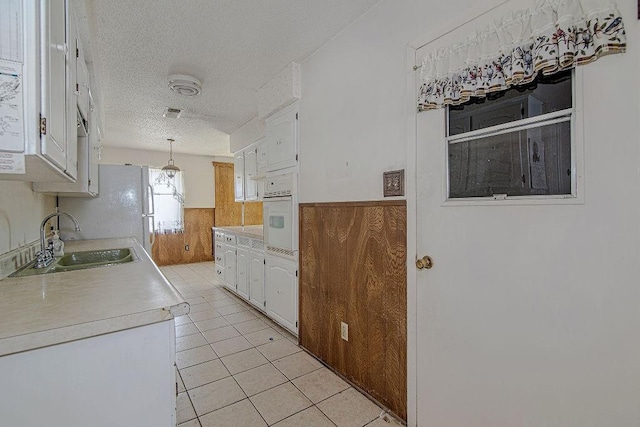 kitchen featuring white appliances, wainscoting, a sink, and white cabinets