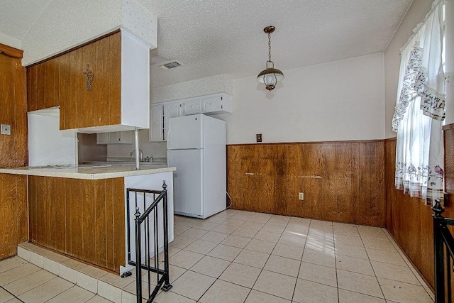 kitchen featuring a wainscoted wall, light countertops, visible vents, freestanding refrigerator, and wooden walls