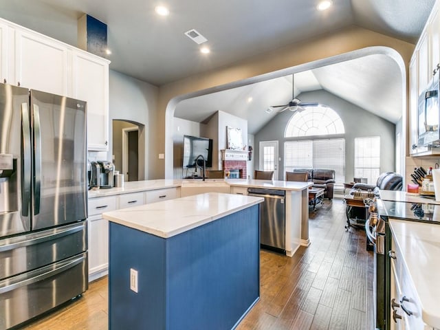 kitchen with stainless steel appliances, a ceiling fan, open floor plan, a kitchen island, and a peninsula