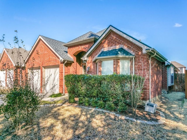 view of front of property with a shingled roof, brick siding, and fence