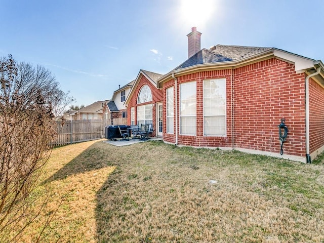 rear view of house featuring brick siding, a chimney, a lawn, a patio area, and a fenced backyard