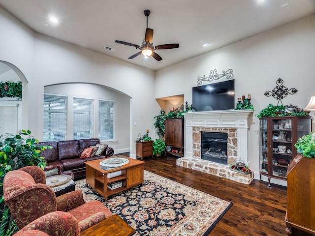 living room featuring a ceiling fan, visible vents, a stone fireplace, and wood finished floors