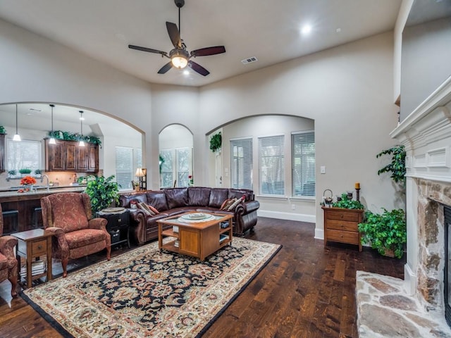 living area with ceiling fan, dark wood-style flooring, a fireplace, and arched walkways