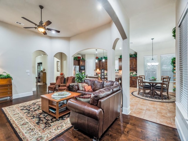 living room with arched walkways, hardwood / wood-style flooring, visible vents, high vaulted ceiling, and ceiling fan with notable chandelier