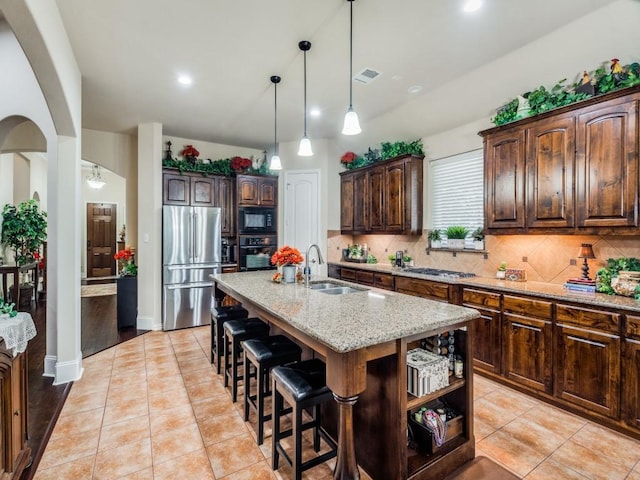 kitchen featuring tasteful backsplash, arched walkways, an island with sink, black appliances, and a sink